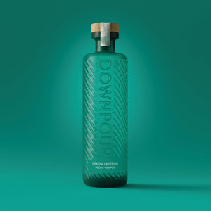 a turquoise bottle embossed with graphic rain pattern and the word DOWNPOUR. It has a wooden stopper and the words 'Coast & Croft Gin' screen printed on it 