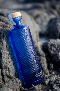 Downpour Scottish Dry Gin. A blue embossed bottle sits leaning against some deep grey rocks. 