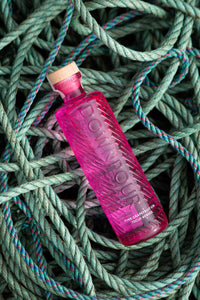 Downpour Pink Grapefruit Gin bottle, lying on a tangle of green ropes